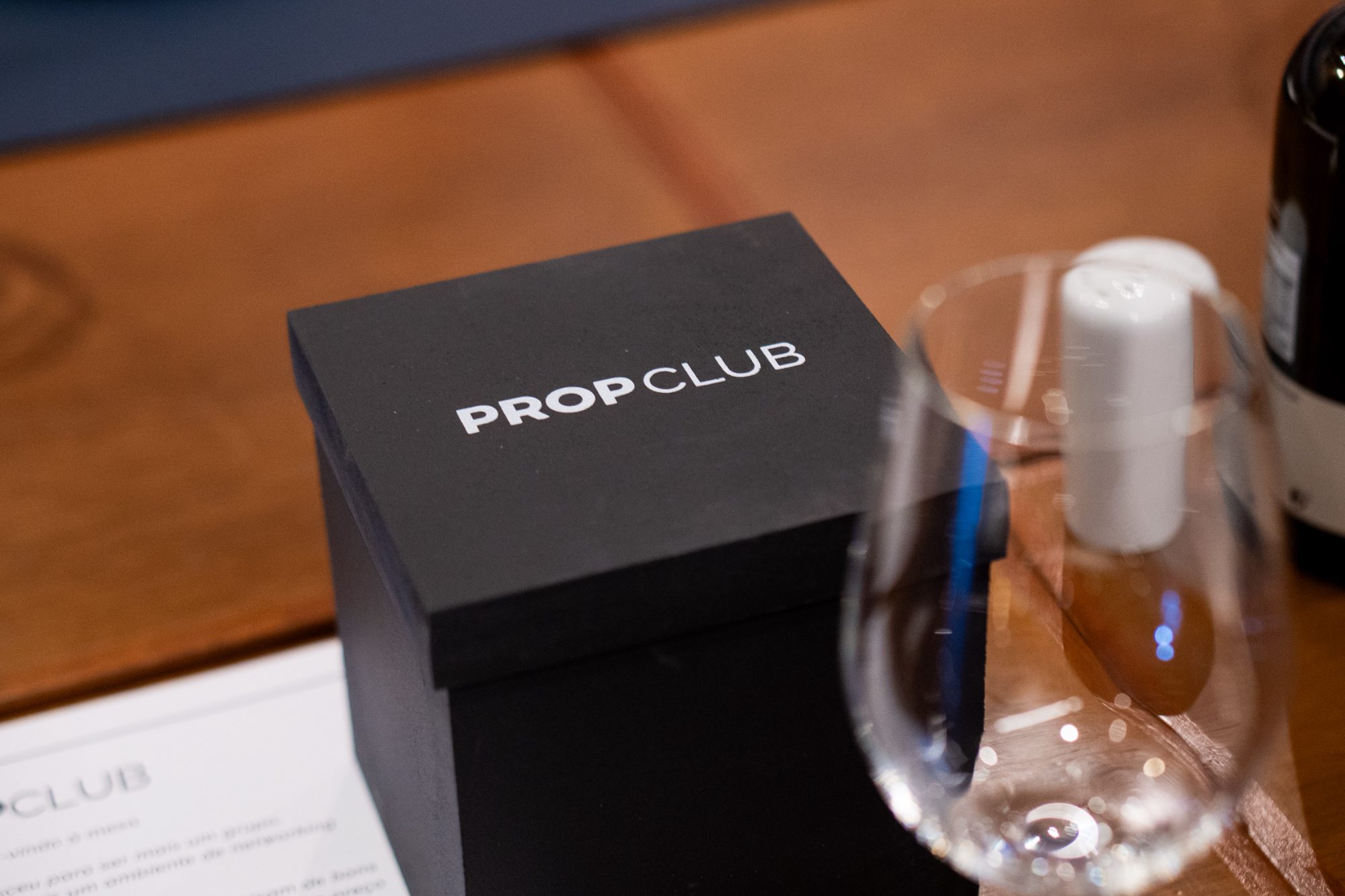Caixa preta PROPCLUB sobre a mesa com taça de vinho